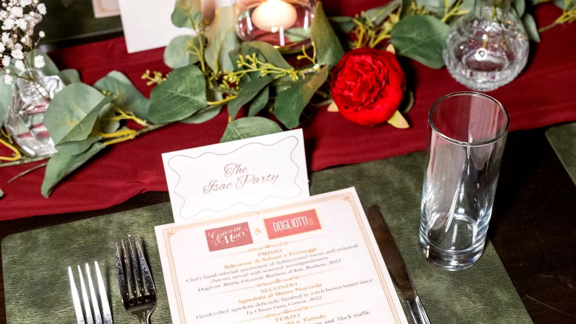 Festive holiday place setting with red and green decor, candles, menu card, and a drinking glass
