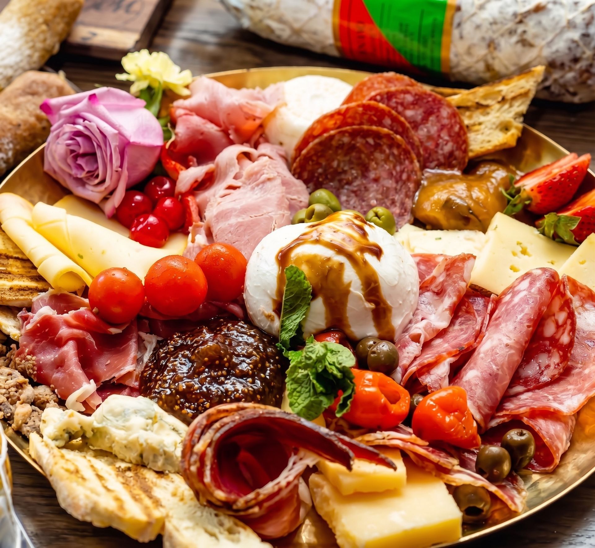 Charcuterie board with cheeses, meats, bread, grapes, cherry tomatoes, and nuts on a wooden platter