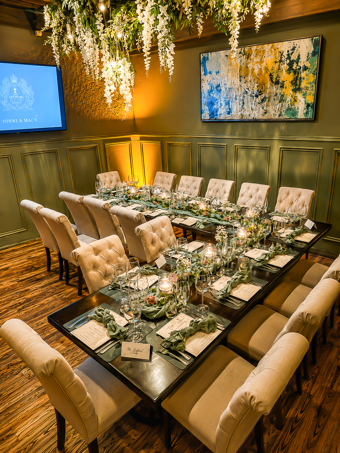Elegant dining table setup in a warm-lit room with hanging greenery and tufted chairs
