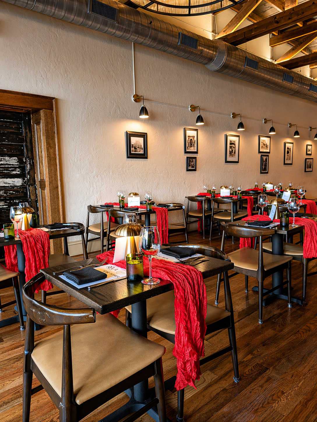 Cozy restaurant dining room with set tables, red napkins, and wall sconces on a warm wooden interior.