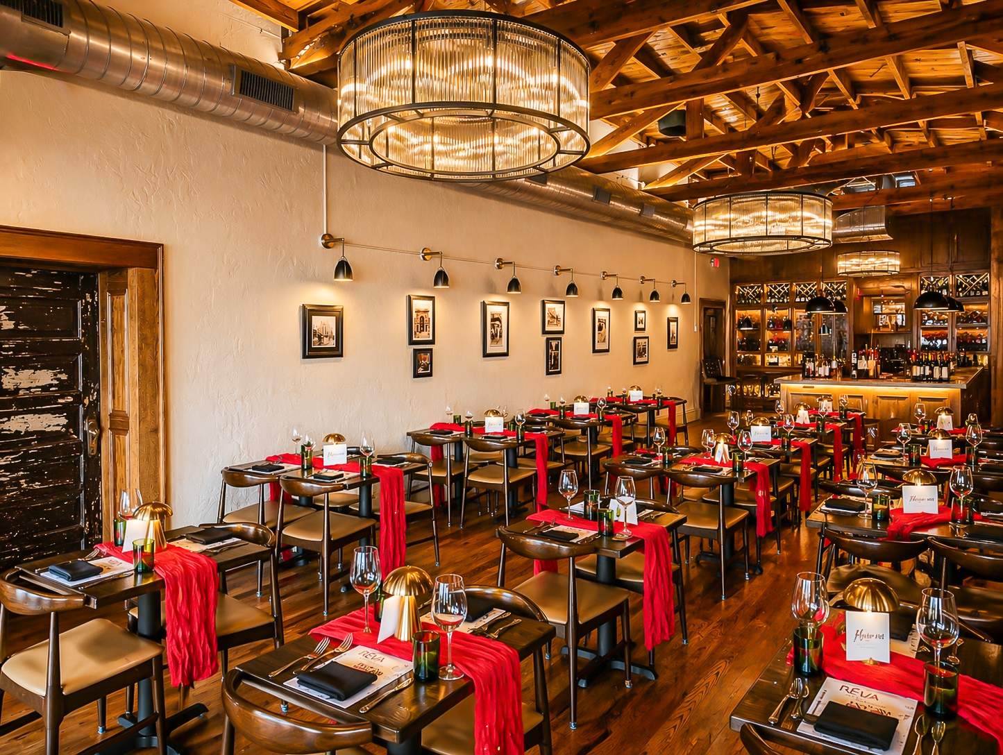 Elegant restaurant dining room with set tables, red accents, chandeliers, and warm wooden decor