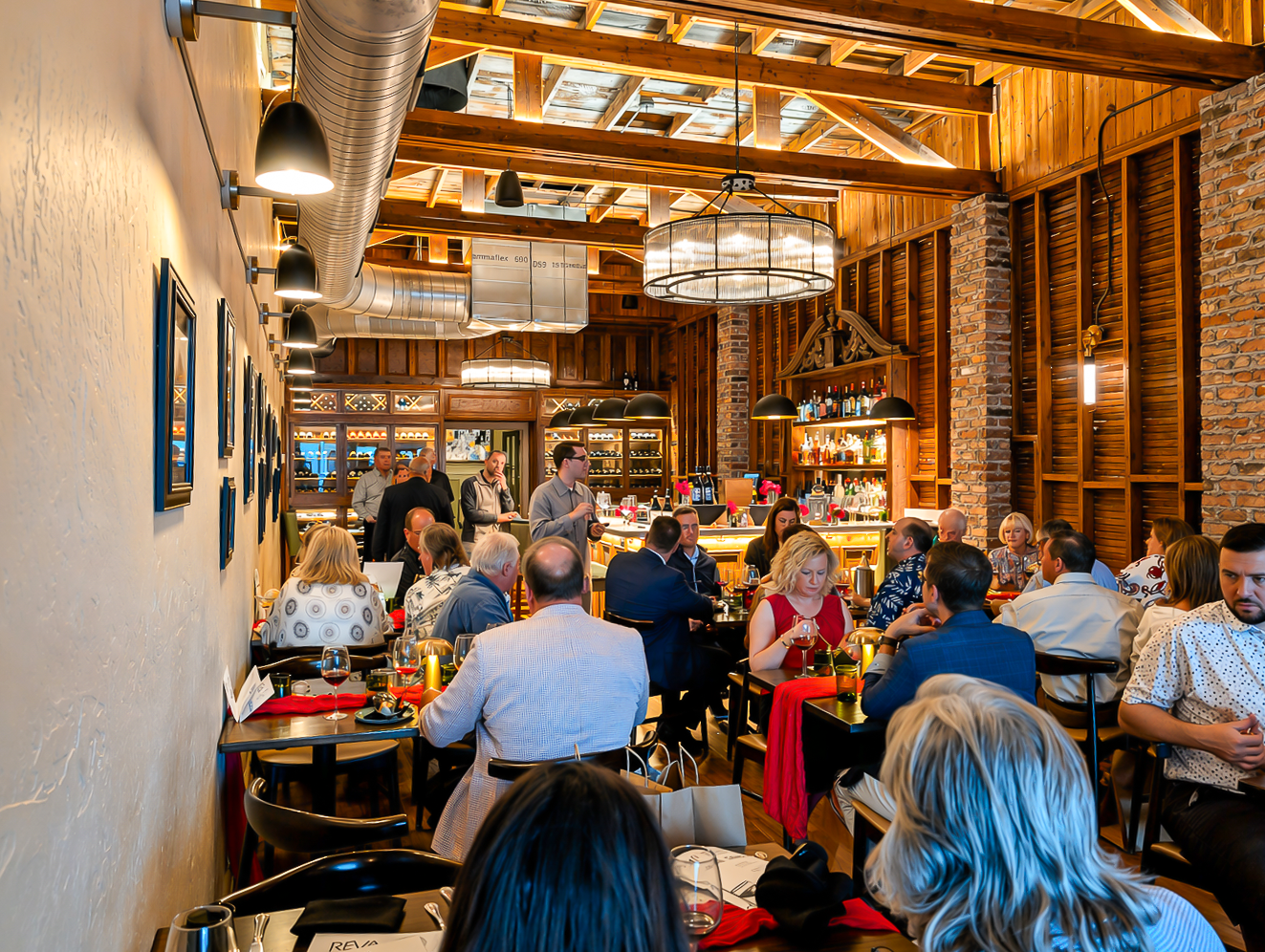 Busy restaurant dining room with exposed wood beams, brick walls, and patrons seated at tables