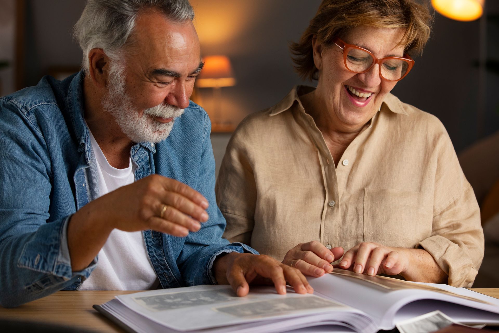 An elderly couple is sitting at a table looking at a photo album.