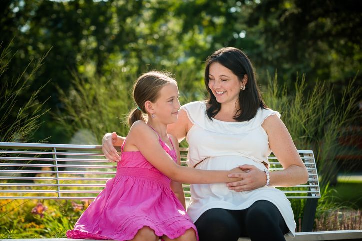A pregnant woman and a little girl are sitting on a park bench.