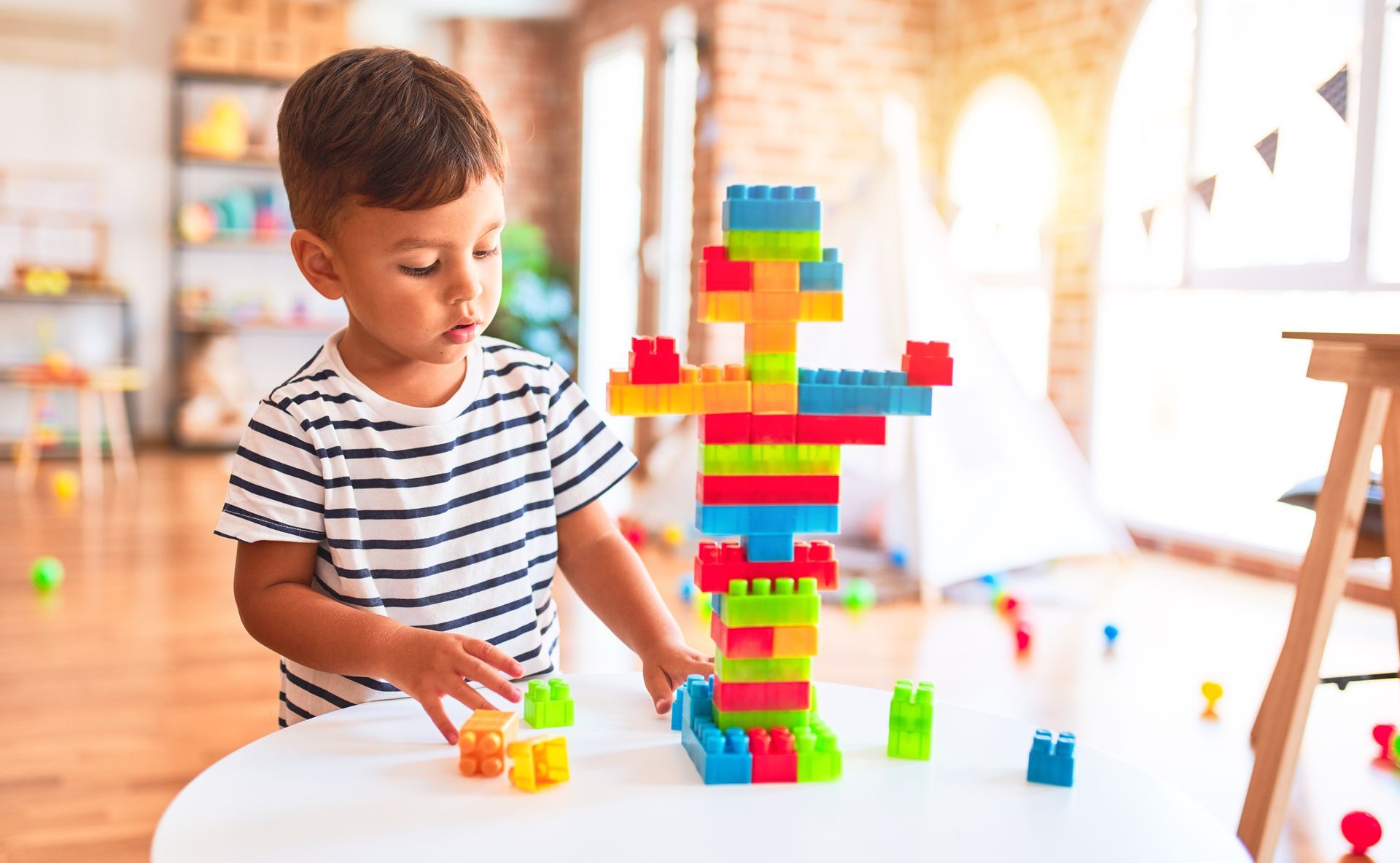 Boy builds tower with colorful blocks on a table.