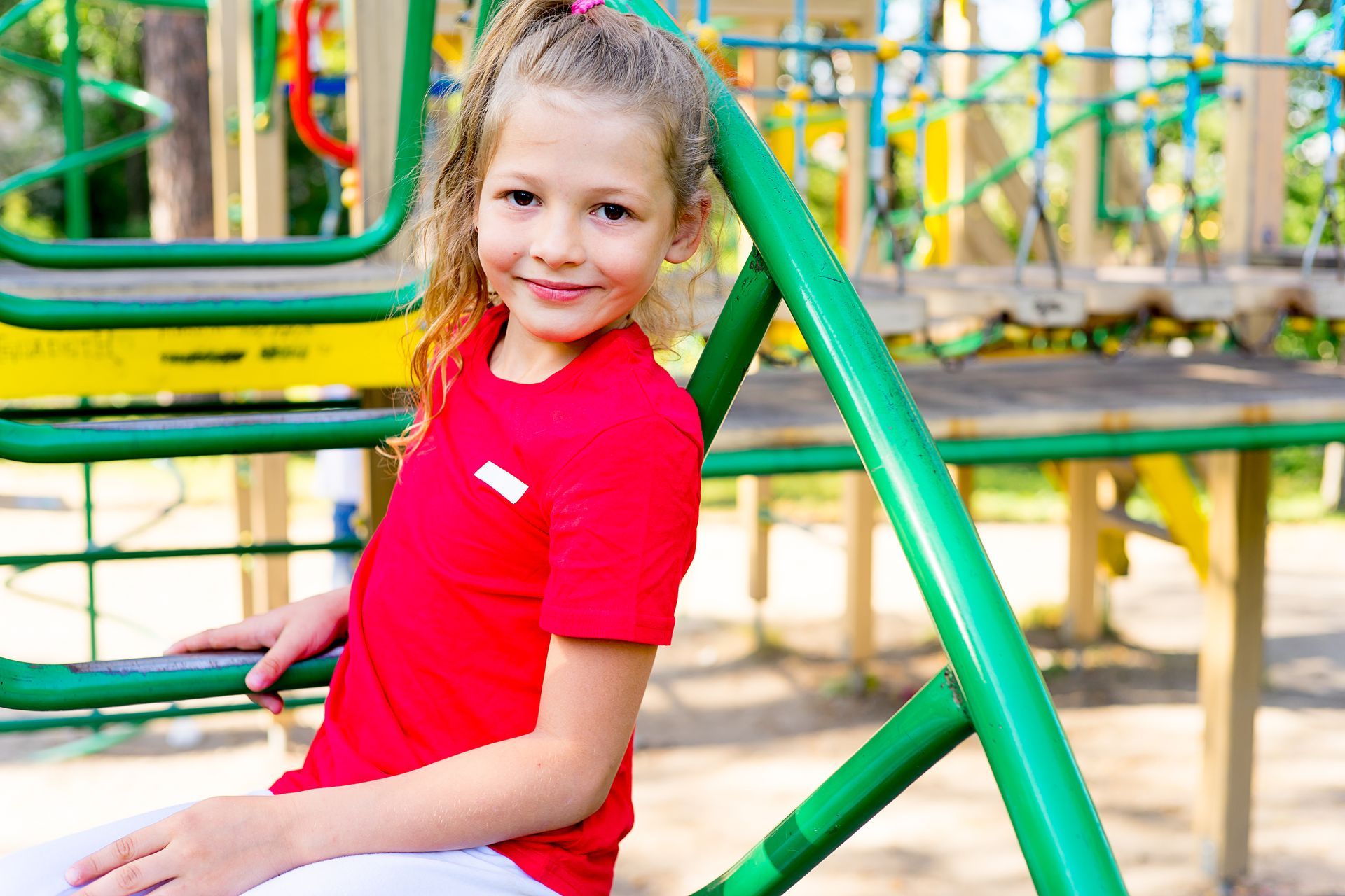 A little girl is sitting on a green railing at a playground.