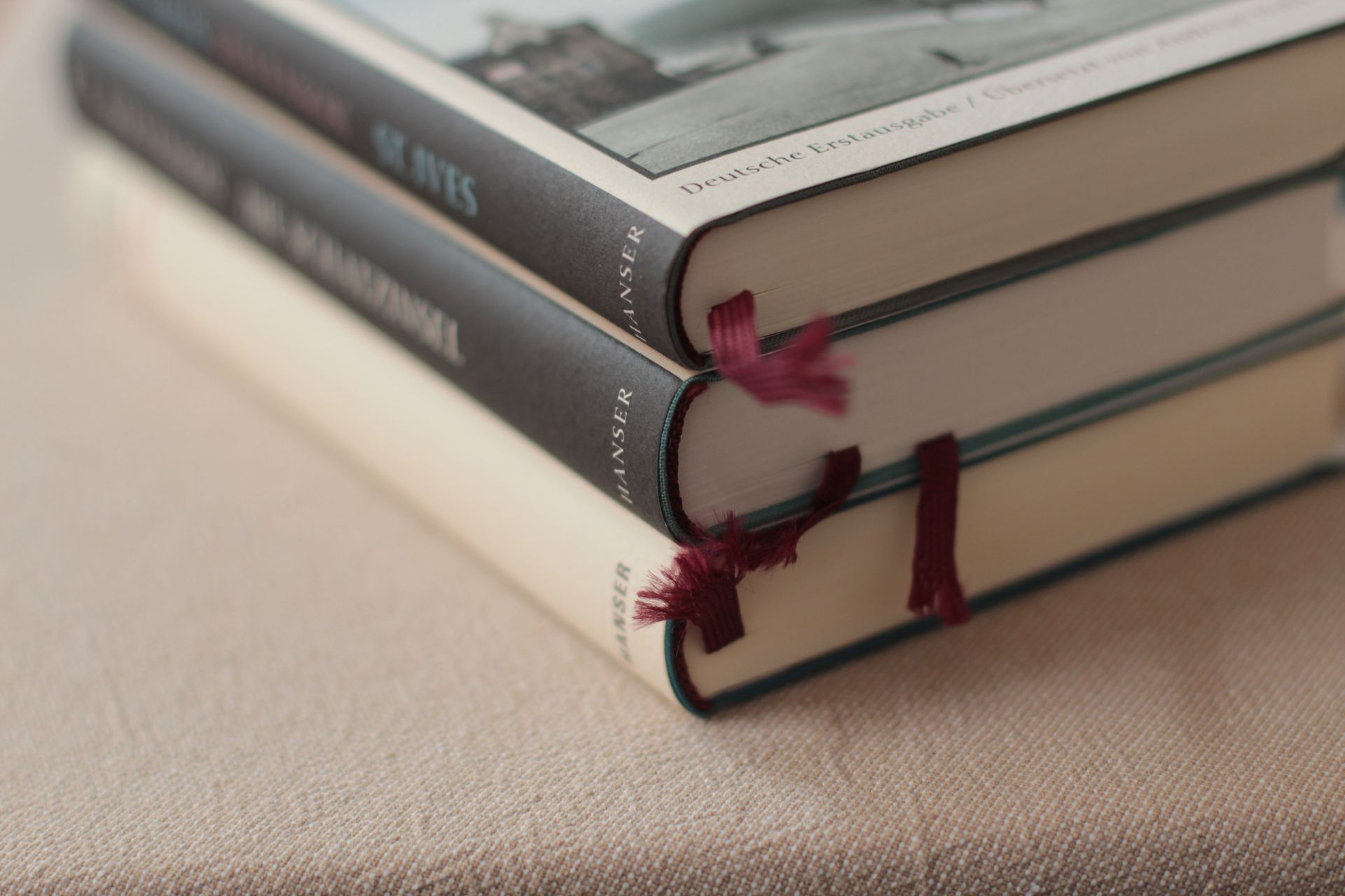 Stack of hardcover books with maroon ribbon bookmarks on a beige surface