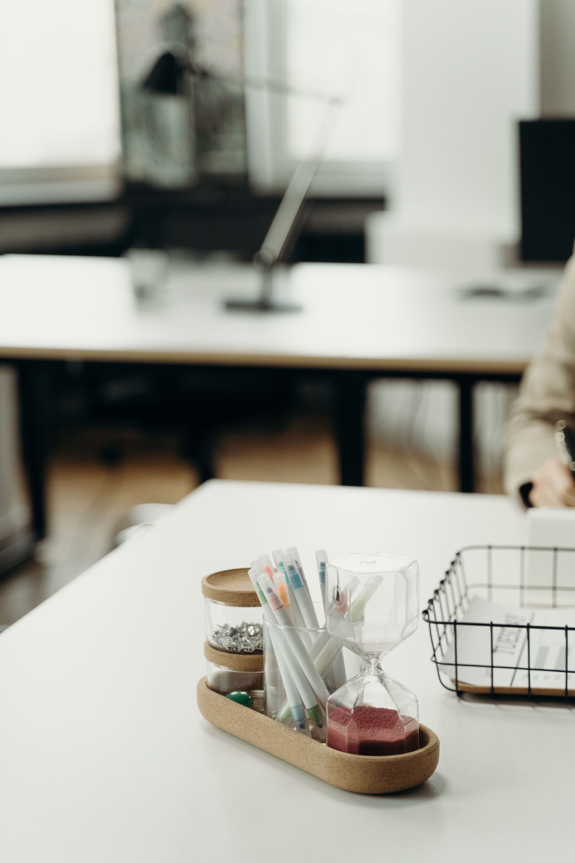 Desk with pen holder and wire tray in a bright office, with a blurred workspace in the background