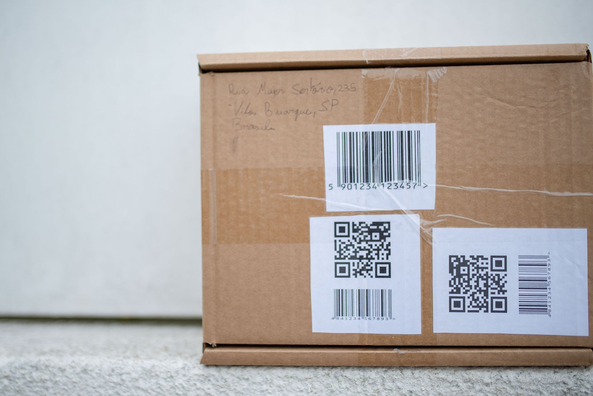 Cardboard shipping box with barcode labels on the floor against a plain wall