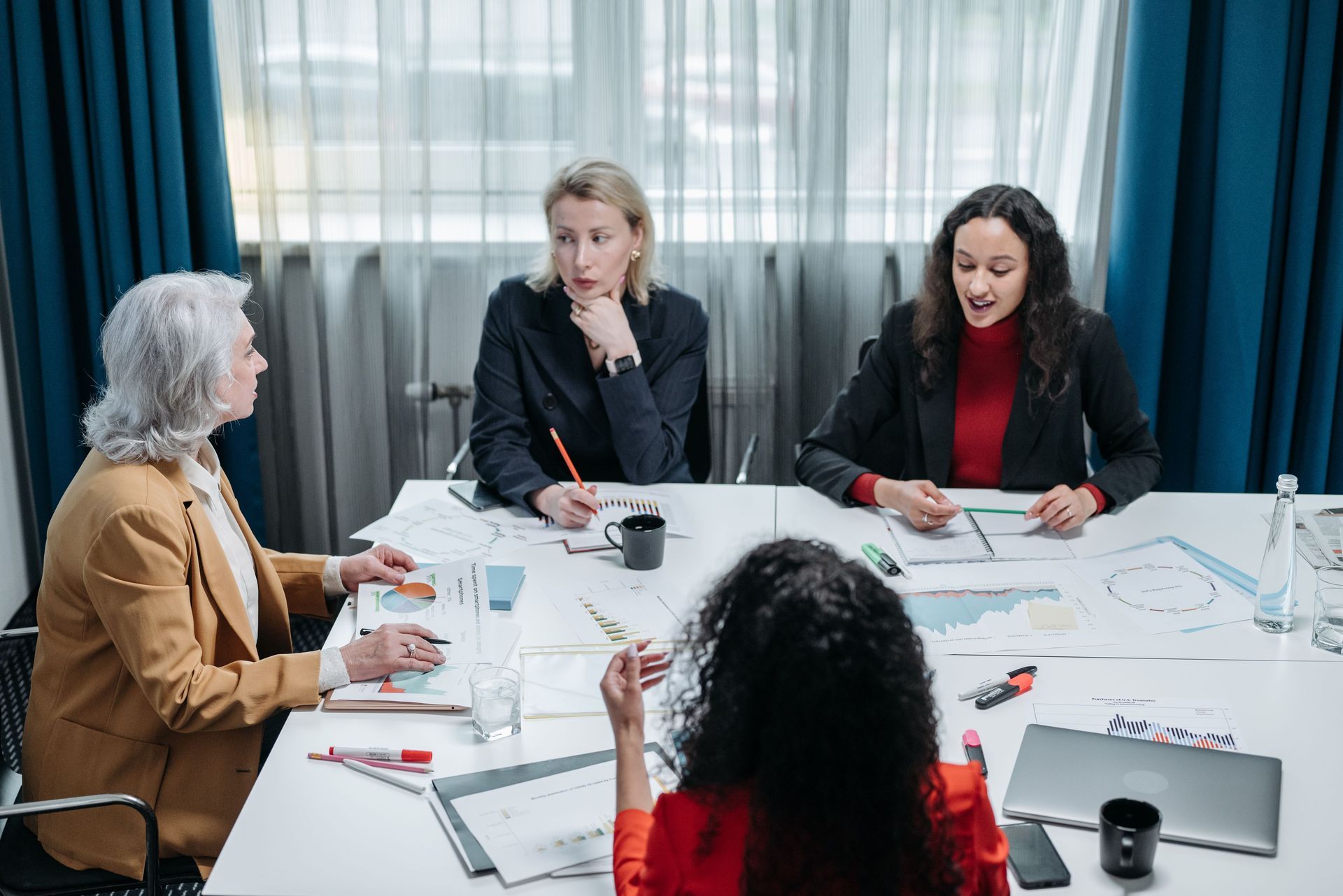 Four people in a meeting around a table, discussing papers in a bright office.