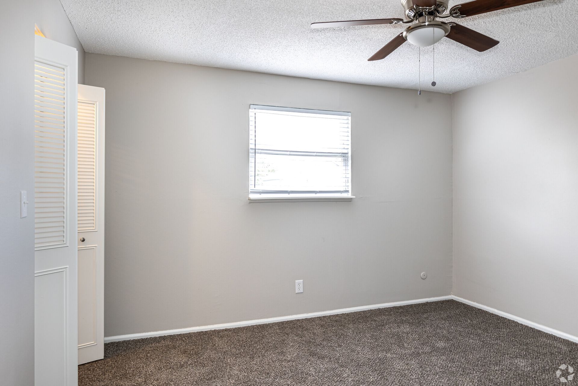 An empty bedroom with a ceiling fan and a window.