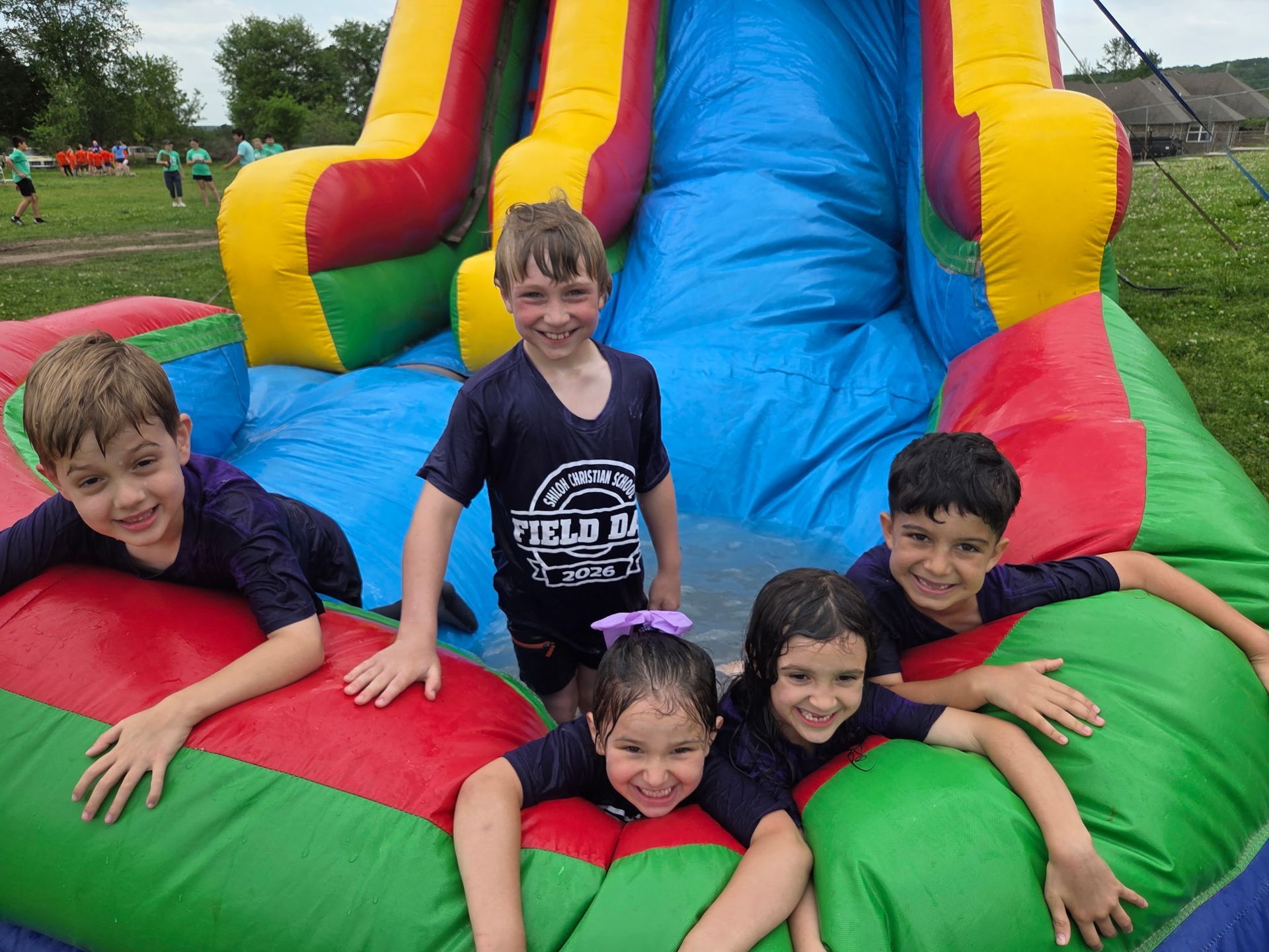 Children smiling on a colorful inflatable slide outdoors, leaning over the red and green base.