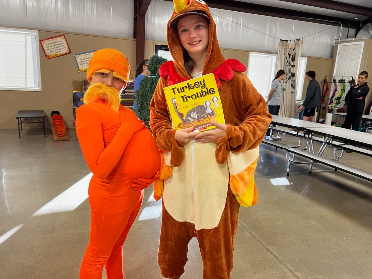 Two people in costumes, one orange Lorax, one turkey, holding a book titled 