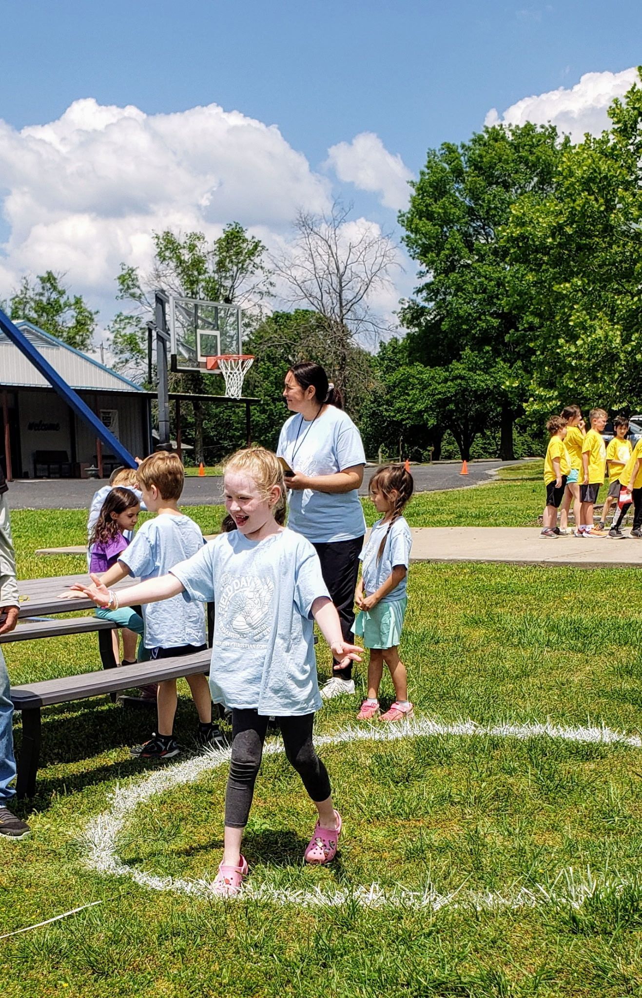 Children playing outside in a grassy area with a teacher. Smiling child in a circle, others watch.