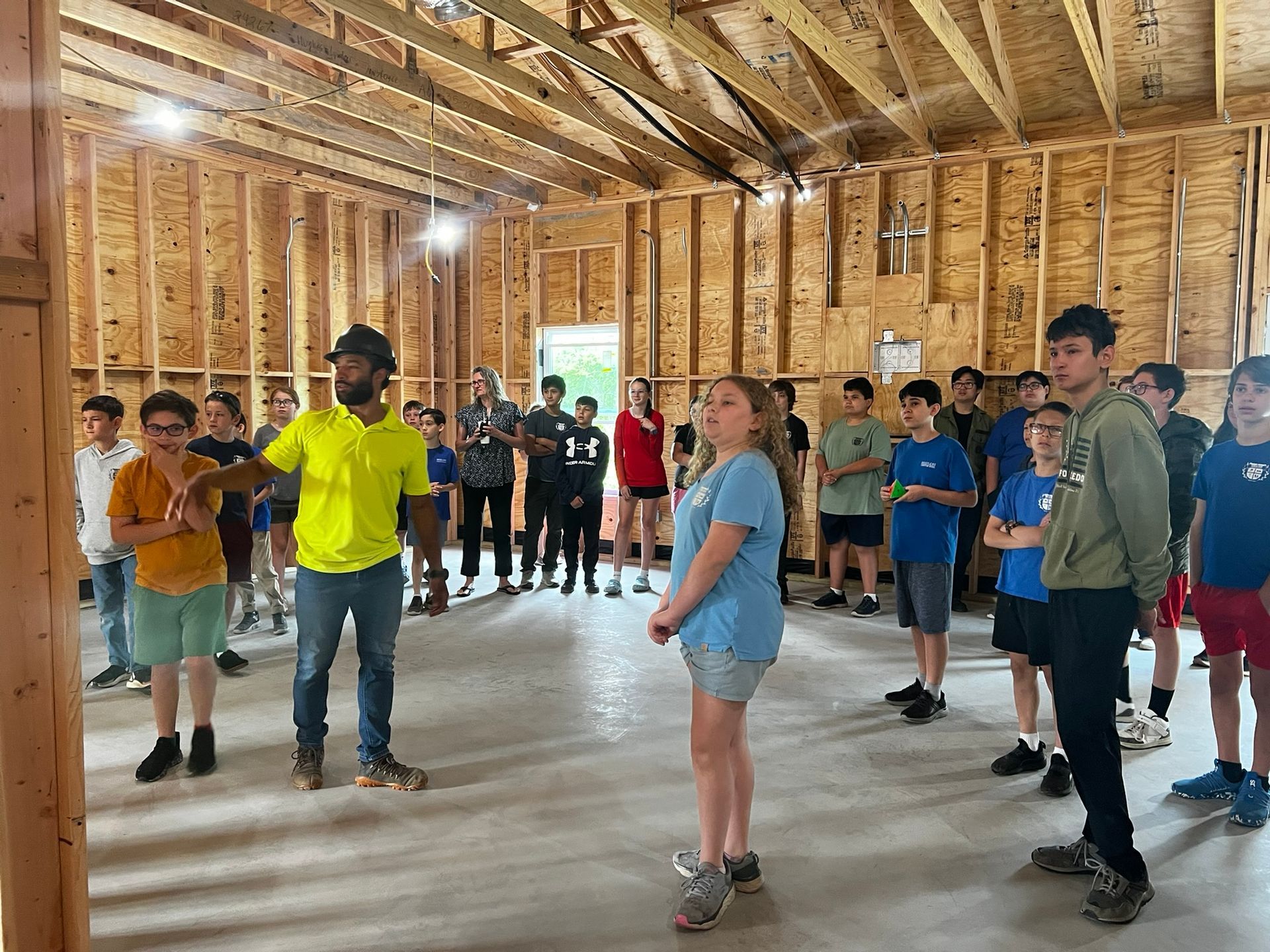 Group of people standing in an unfinished wooden building, appearing to listen or wait during an indoor gathering