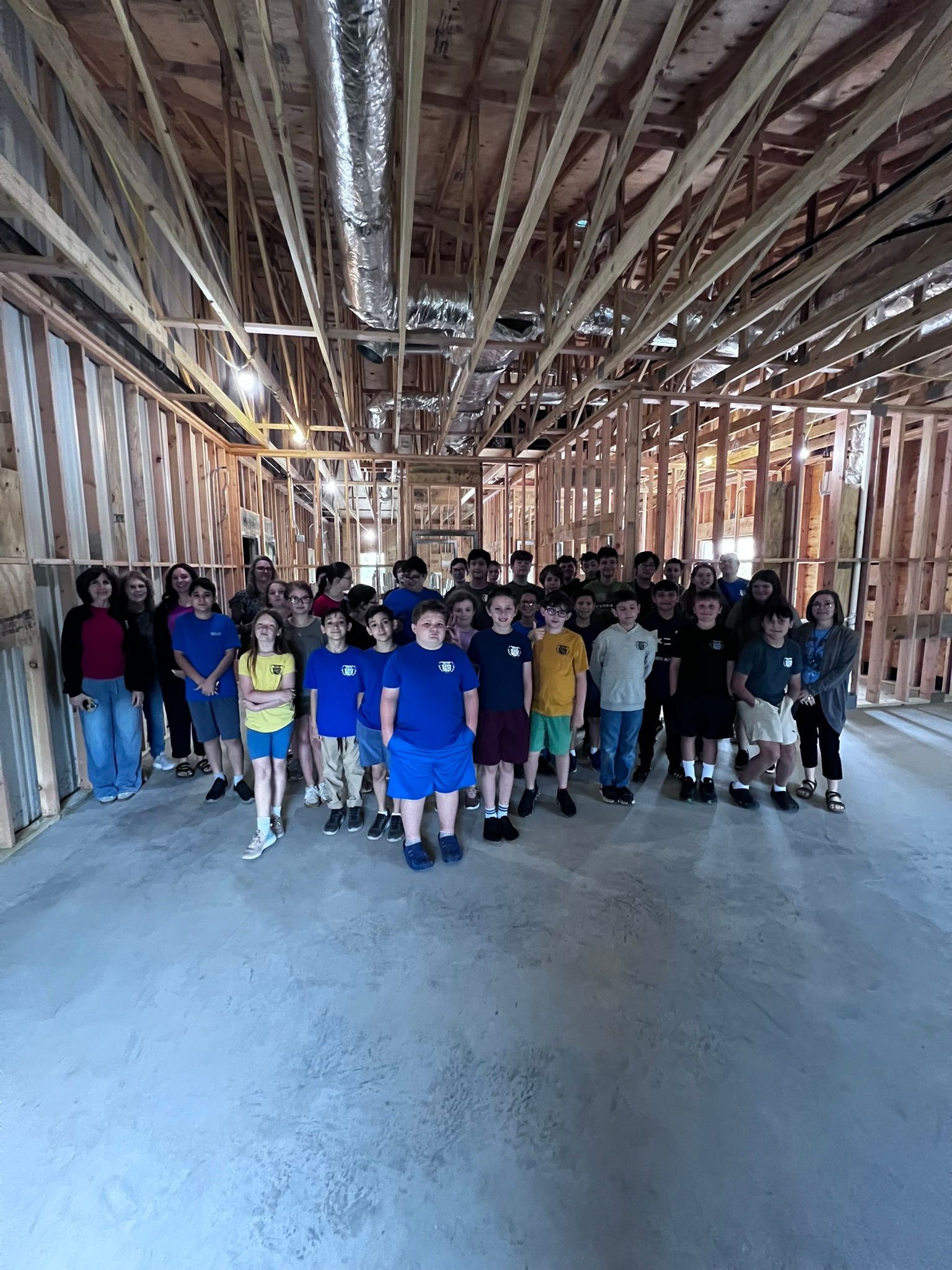 Group of people standing together in an unfinished wooden building with exposed ceiling beams.