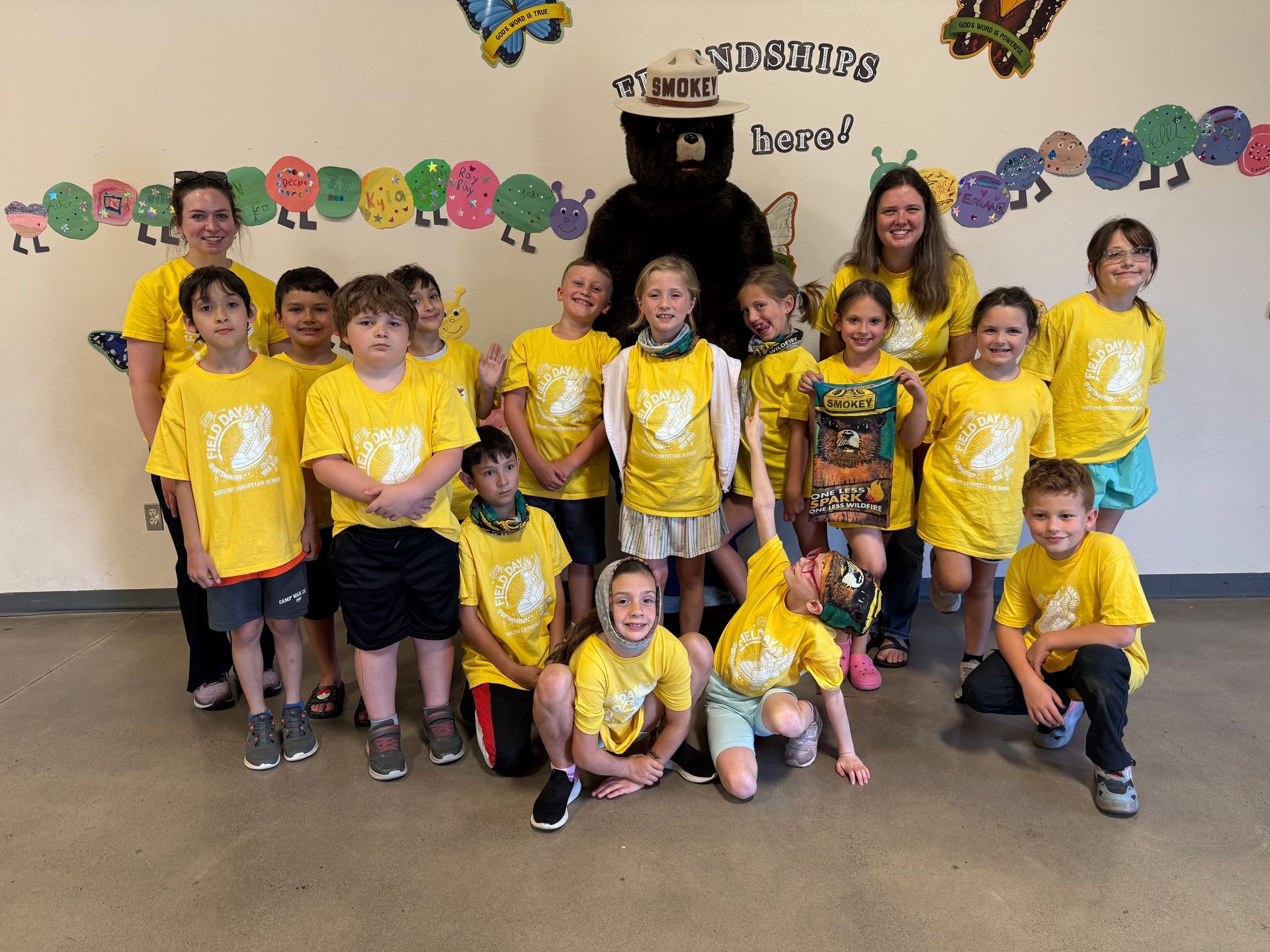Group of kids in yellow shirts pose with Smokey Bear and two adults.
