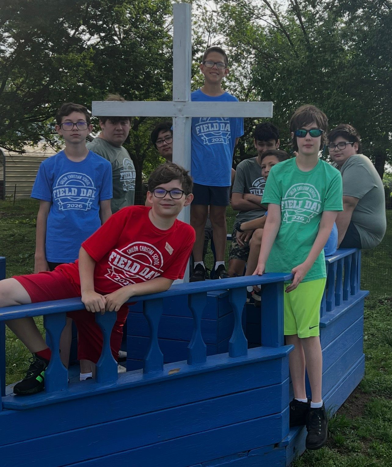Group of people posing on a blue wooden bridge, wearing colorful T-shirts outdoors.