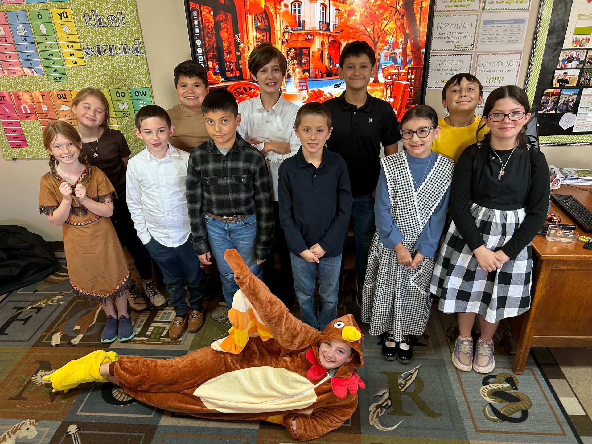 A group of children are posing for a picture in a classroom . one of the children is dressed as a turkey.
