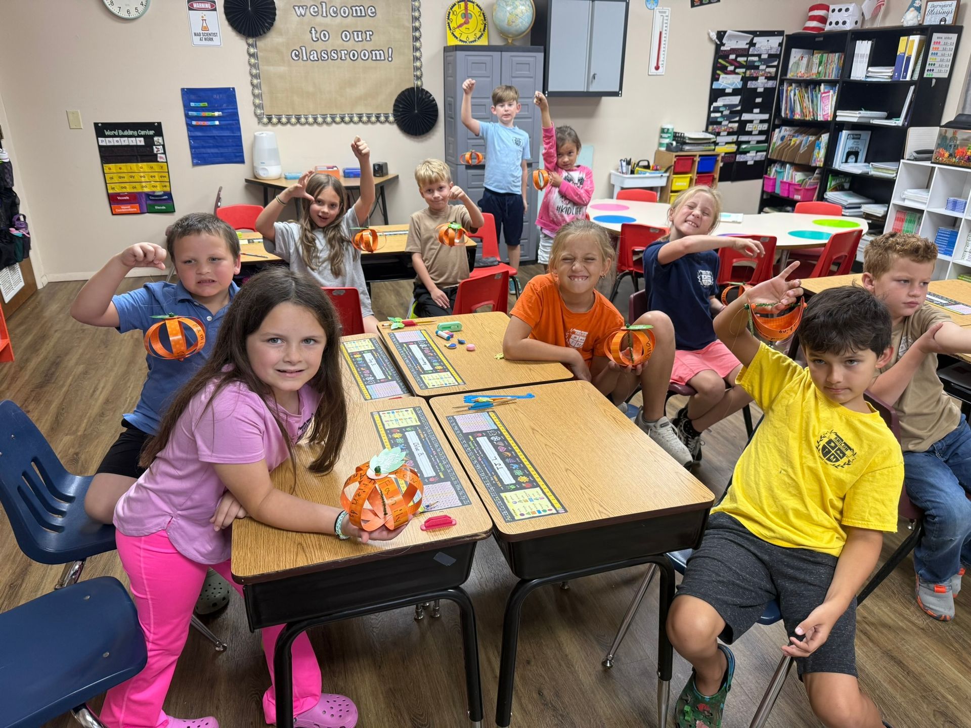 Classroom of children with pumpkins, flexing, smiling at desks.