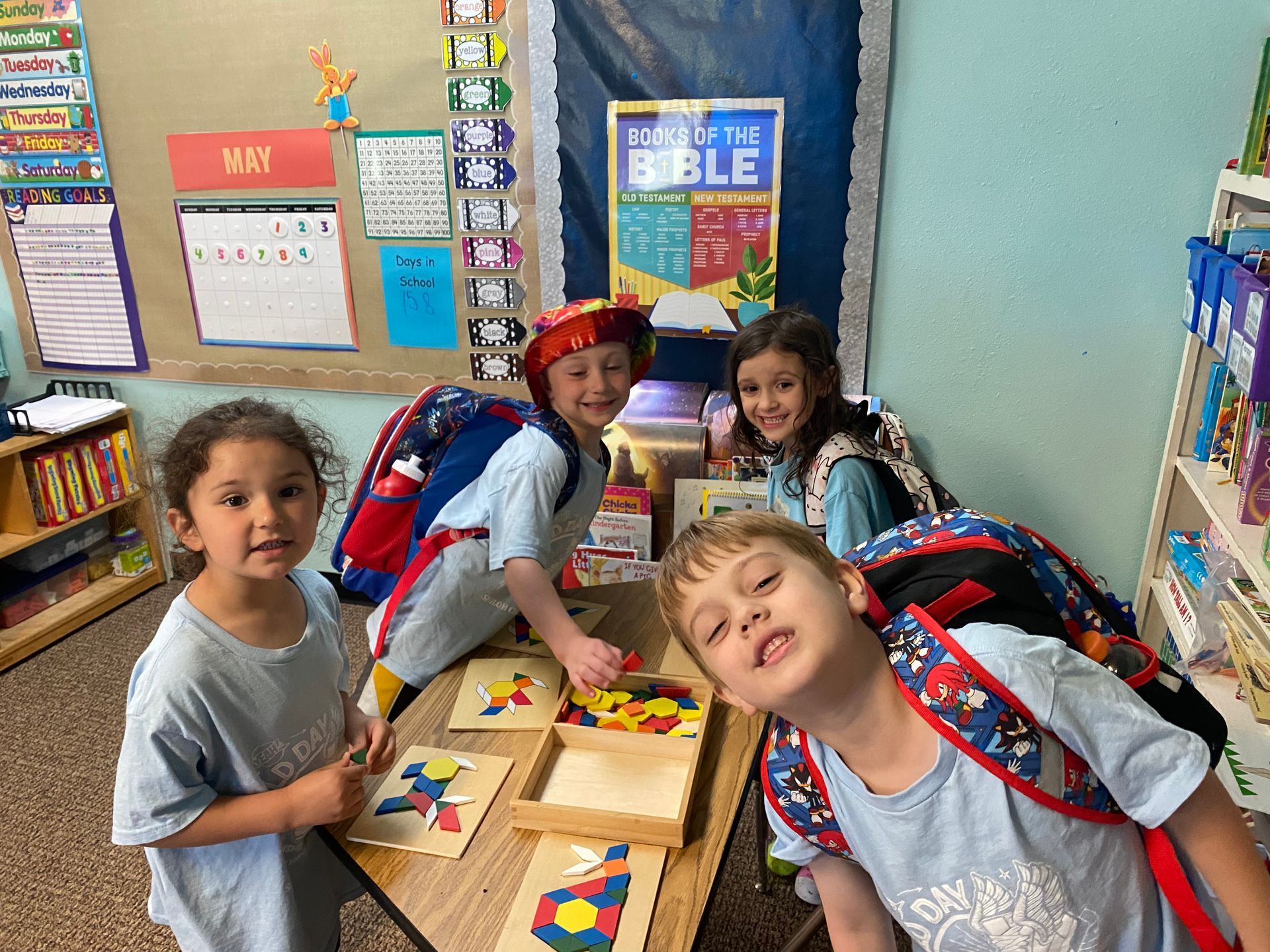 Four children smile while playing with colorful shapes in a classroom.