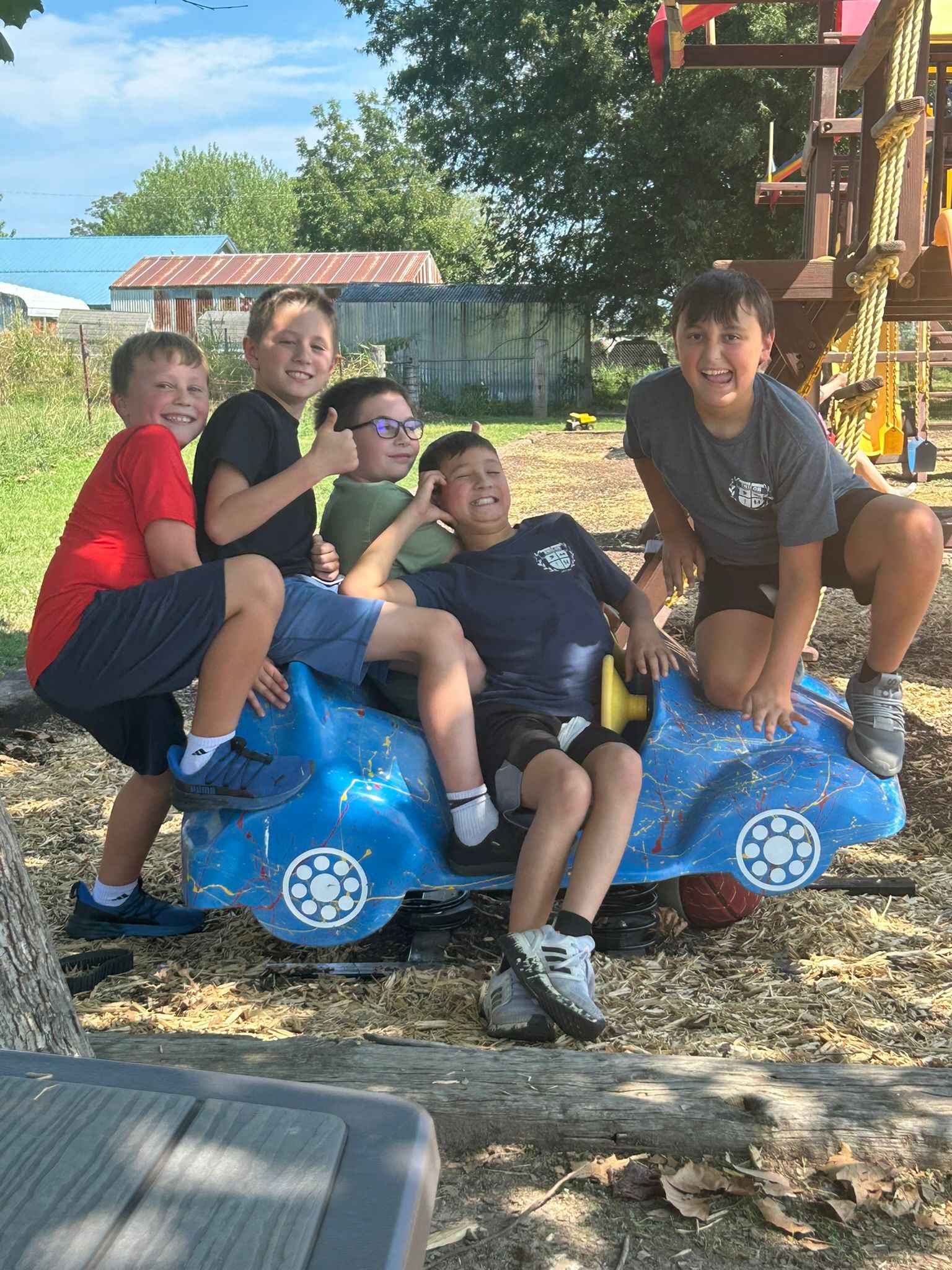 Group of boys on a blue playground car, smiling and posing in a park.