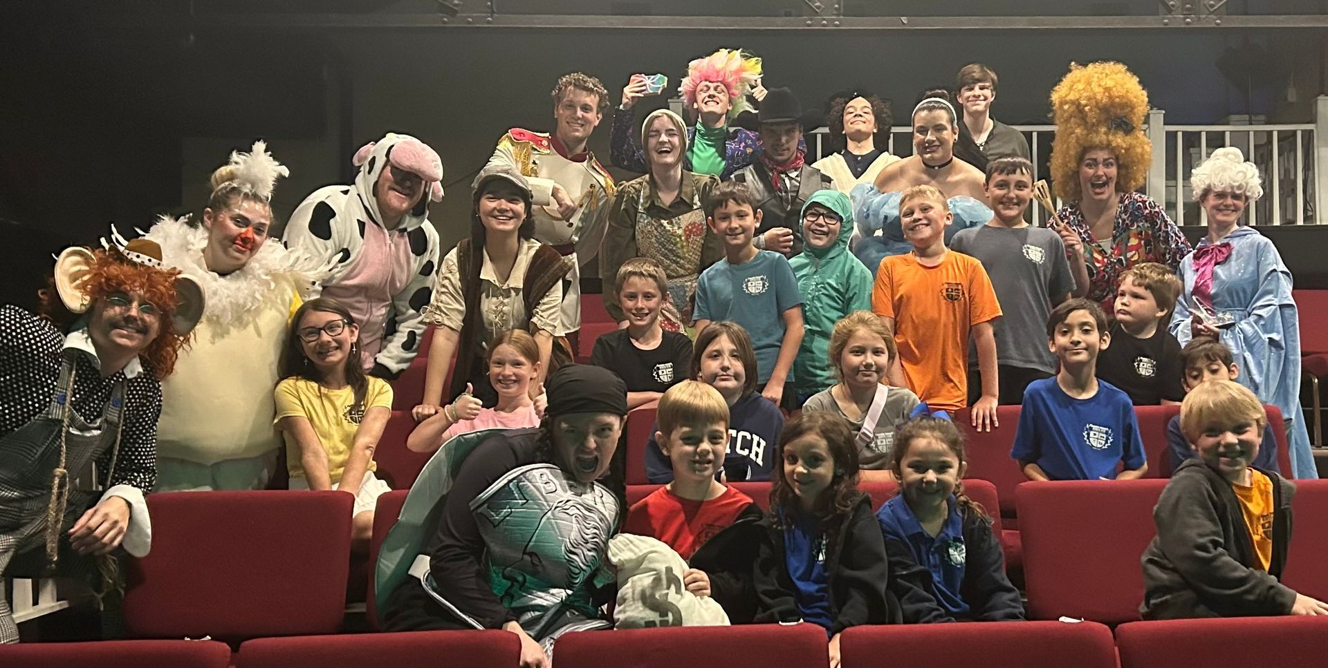 A group of people in costumes smiling in an auditorium.