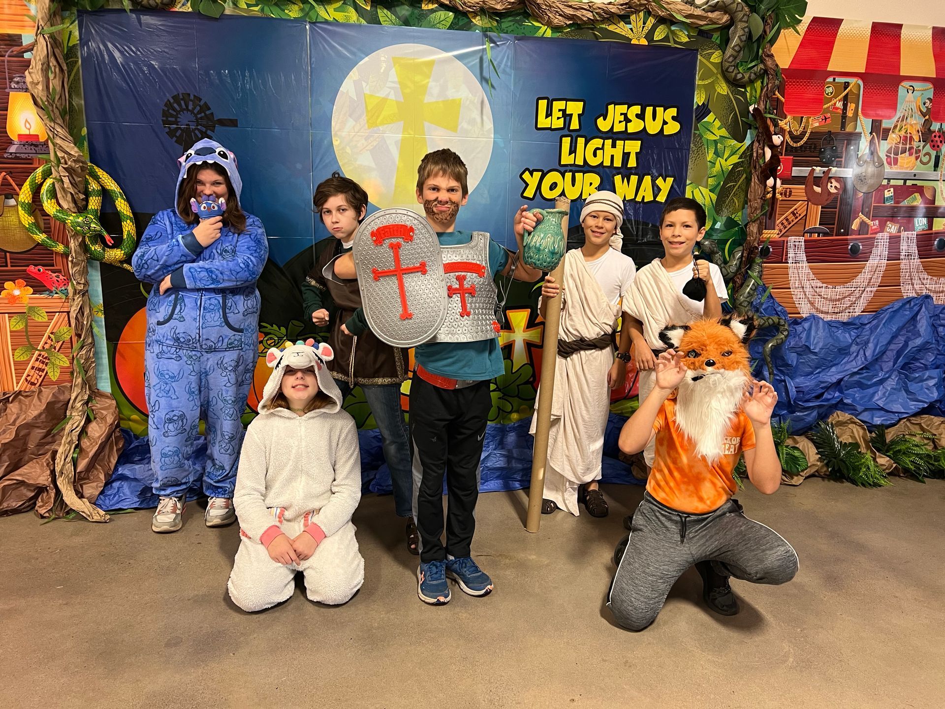 A group of children are posing for a picture in front of a sign that says let jesus light your way.