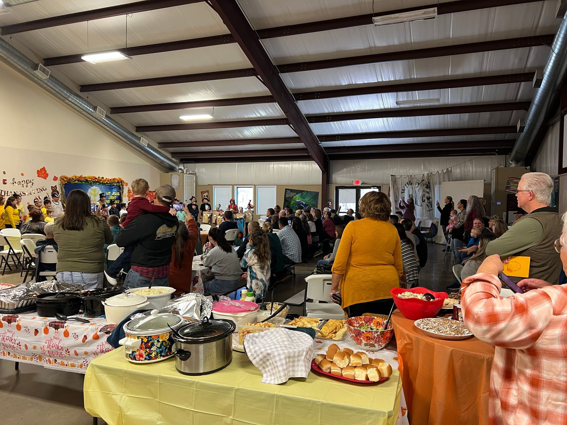 A large group of people are standing around tables filled with food.
