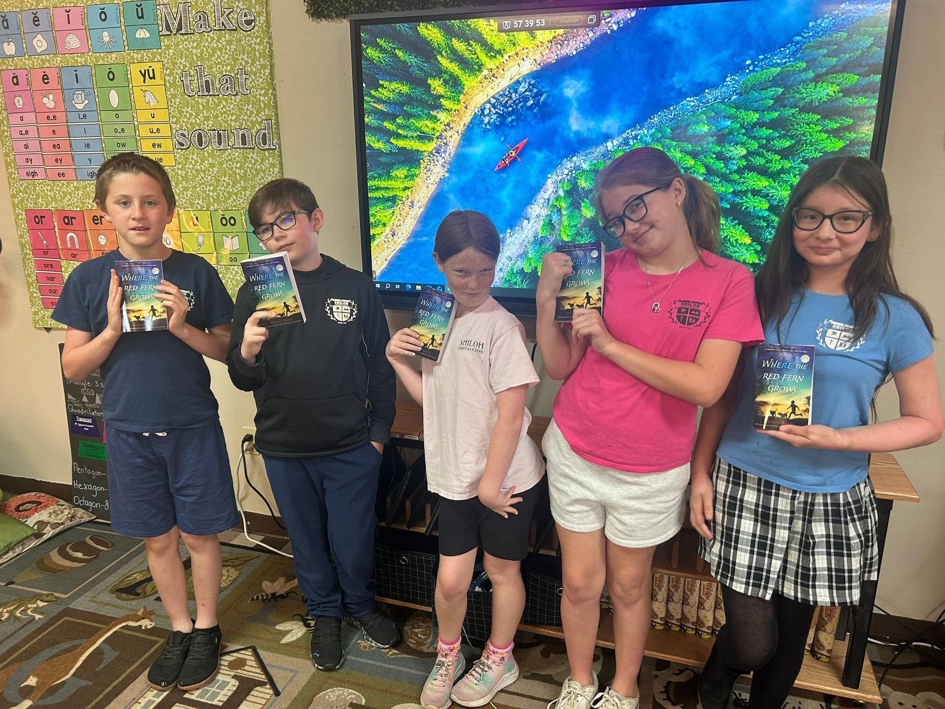 Five students holding certificates stand in a classroom in front of a colorful mural.