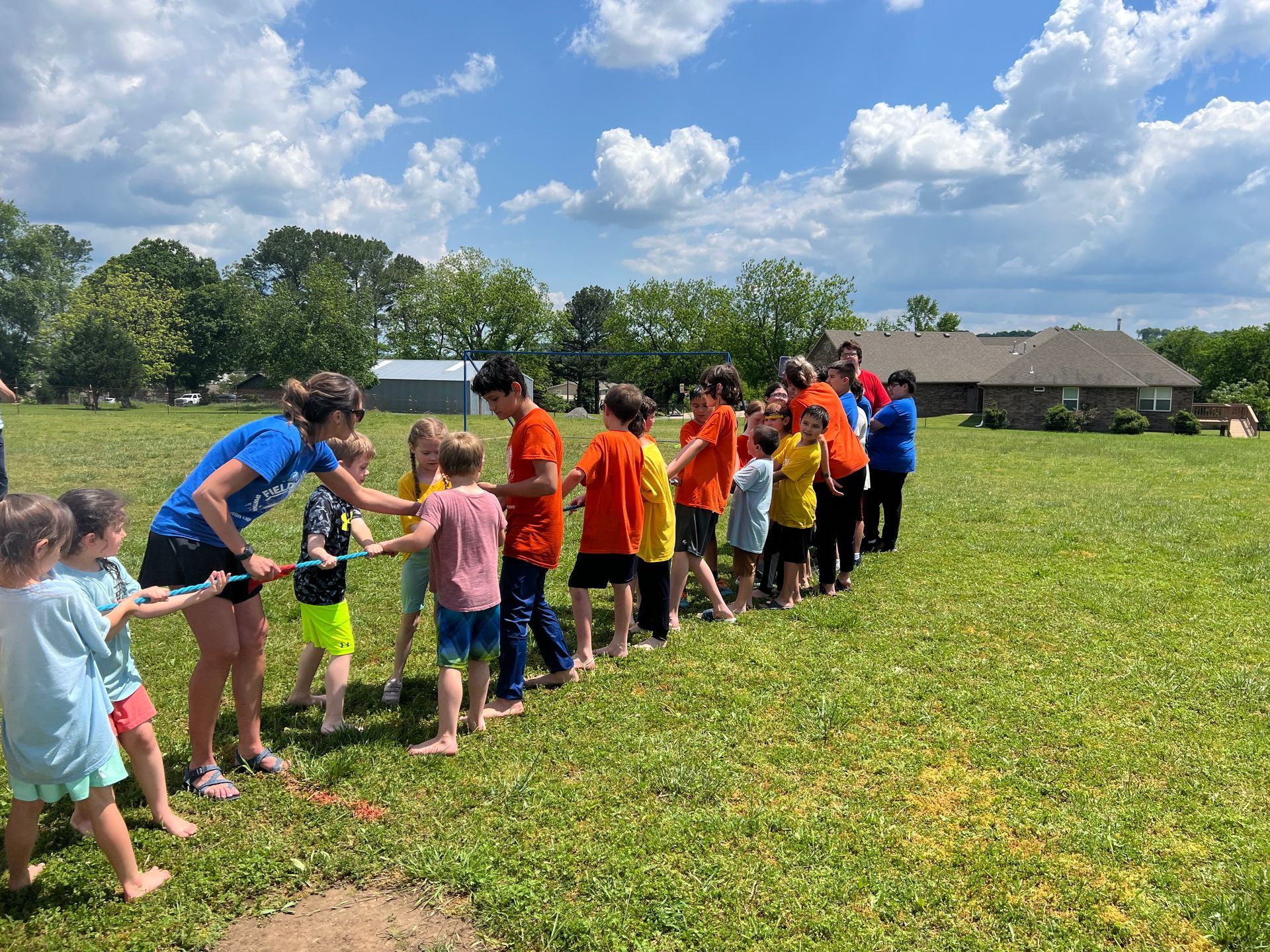 Children playing tug-of-war on grass under a blue sky. Two teams, colorful clothes, pulling a rope.