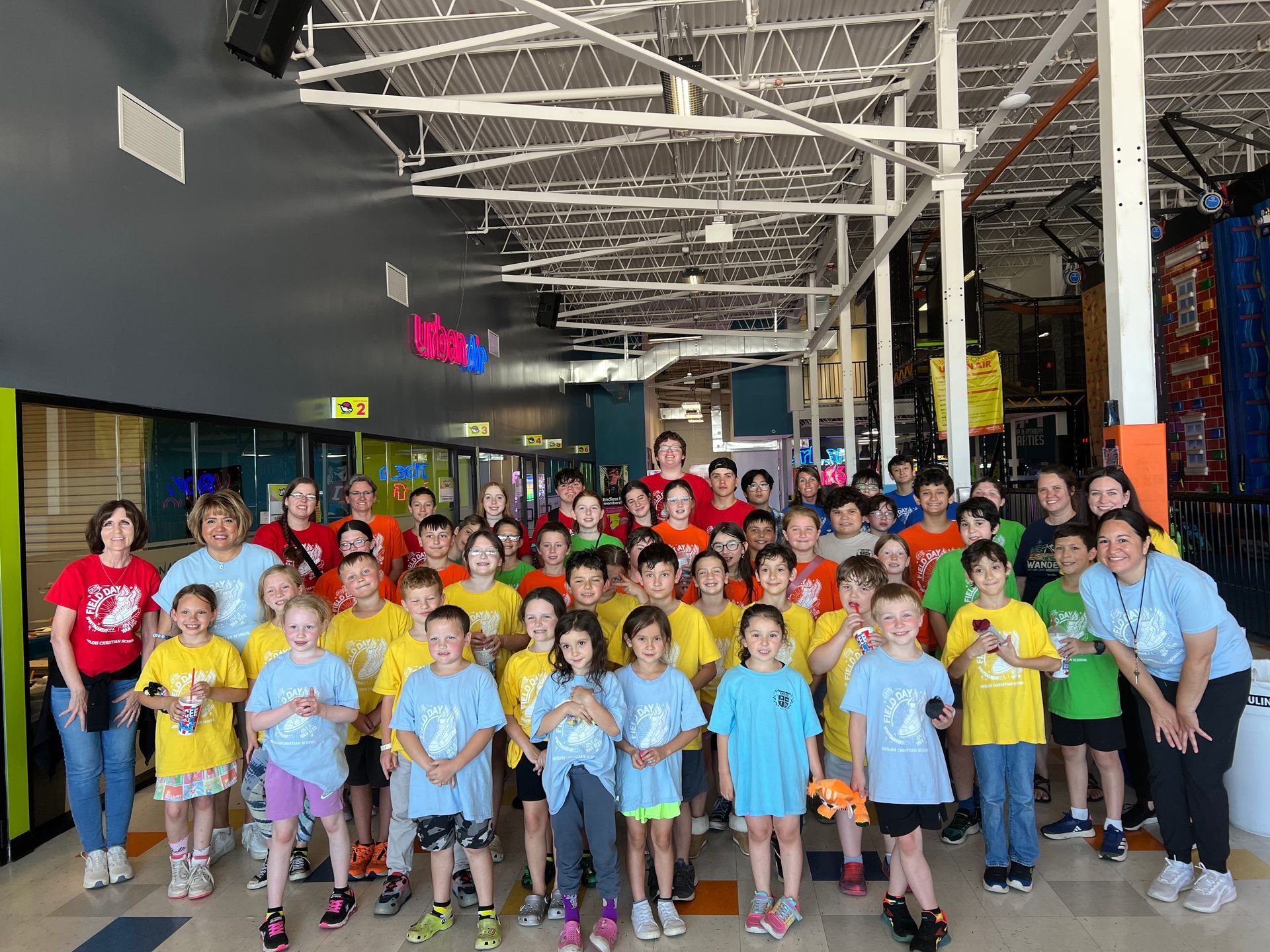 Group of children and adults in colorful shirts posing indoors, possibly at an entertainment venue.