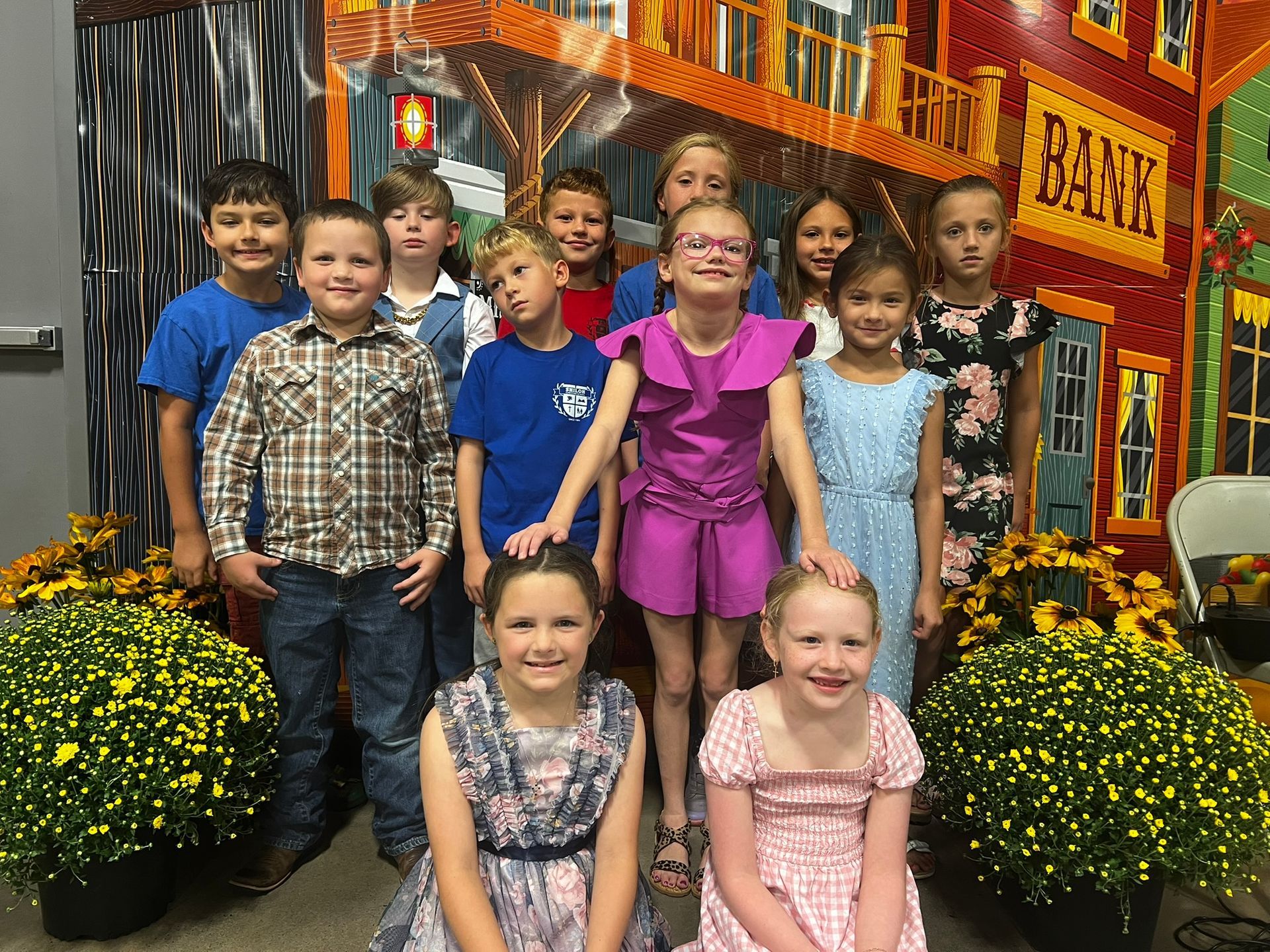 Group of children posing in front of a colorful western-themed backdrop. Smiling, dressed up, and ready for an event.