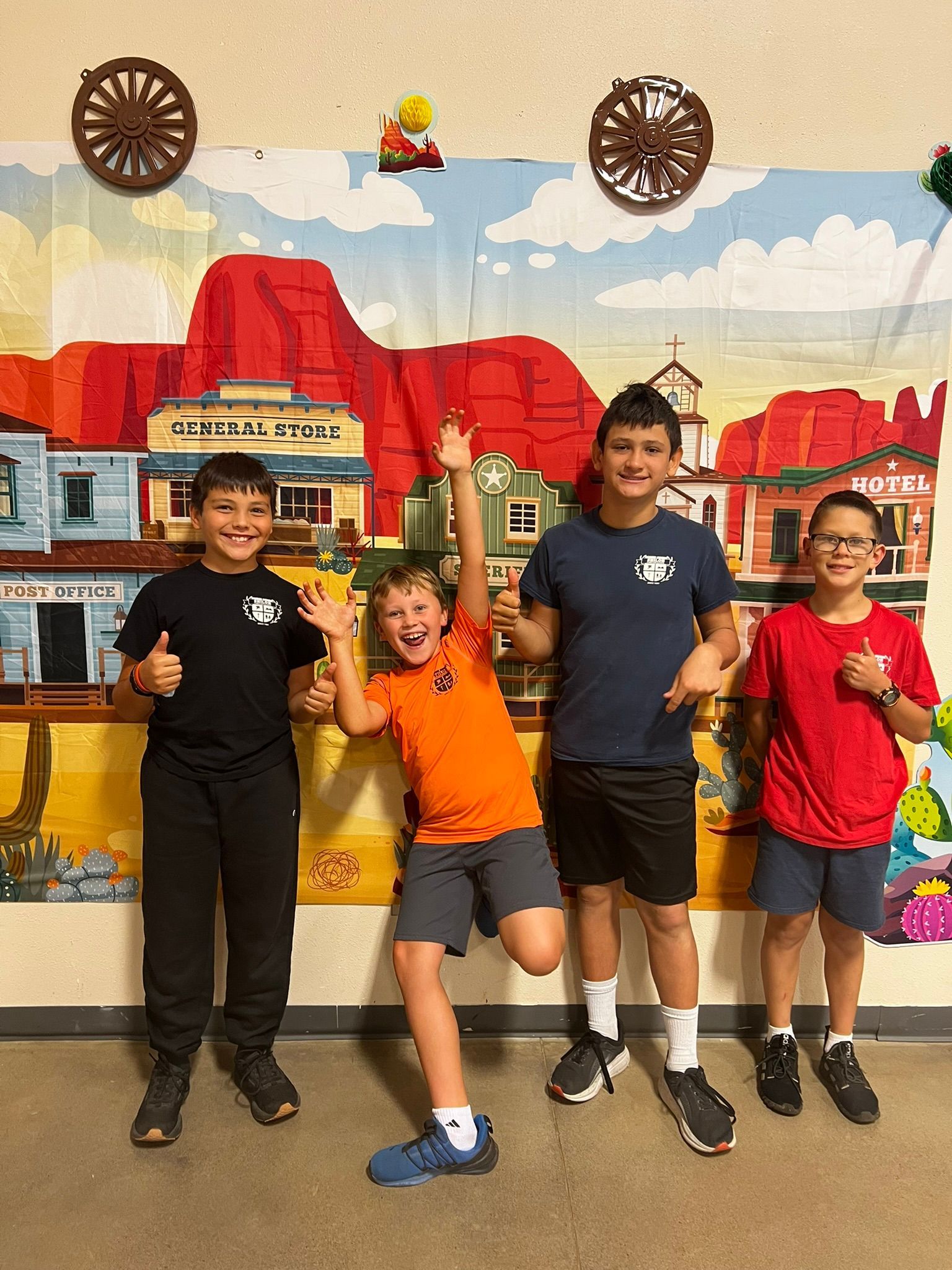 Four boys smiling and posing in front of a Western-themed mural.