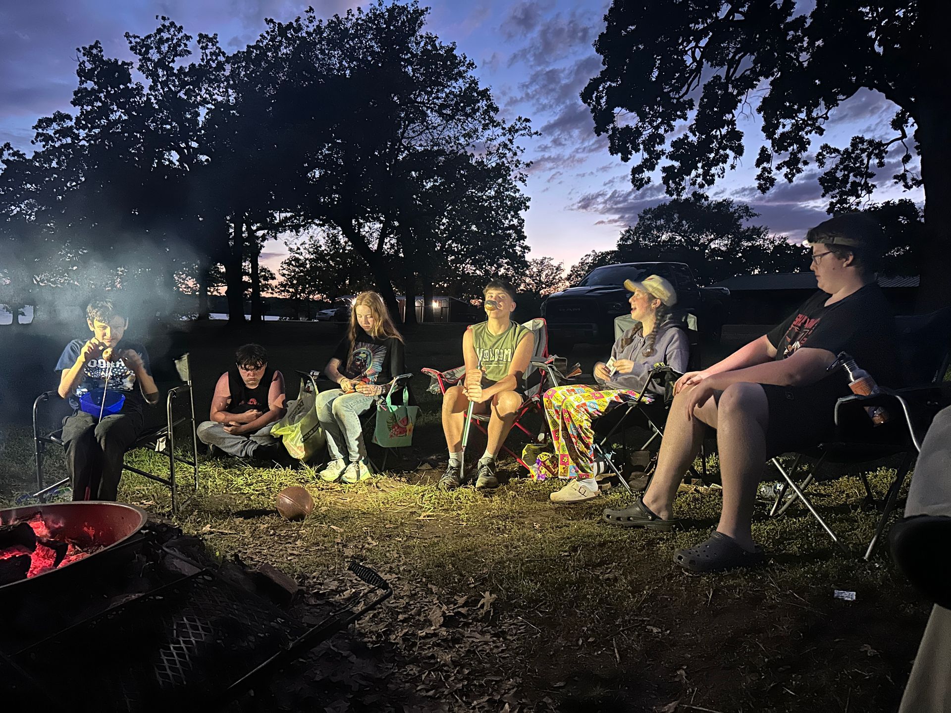 Group of people sitting around a campfire outdoors at dusk.