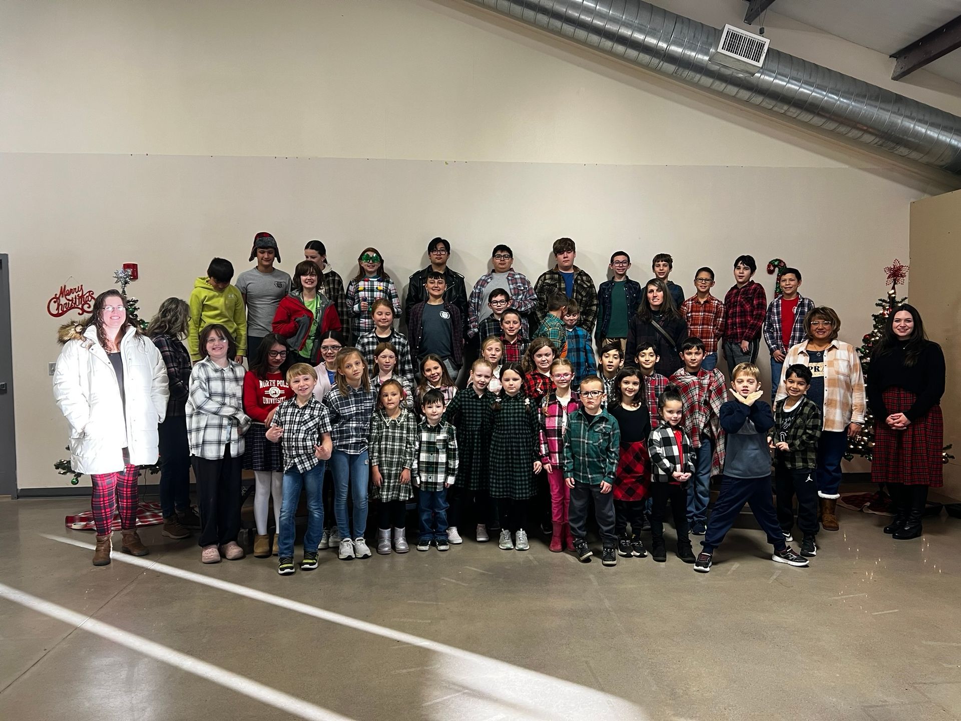 Group of children and adults posing indoors, many wearing plaid.