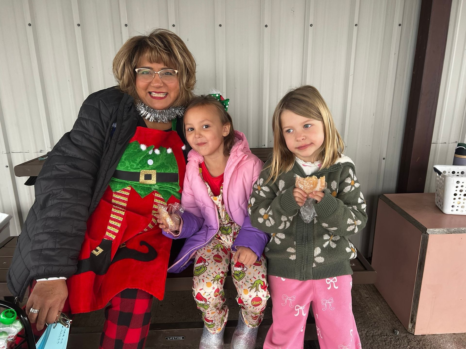 Woman in Christmas apron with two young girls eating snacks, outside.