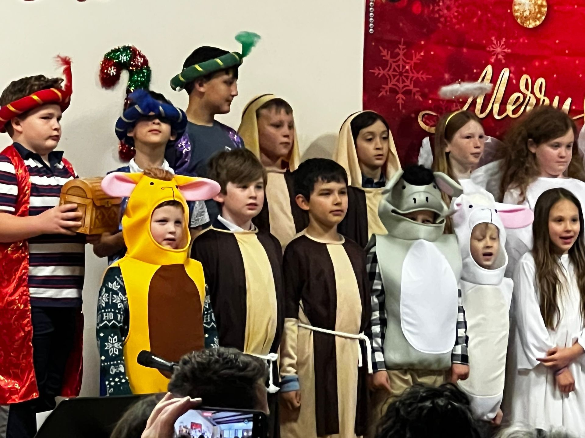Children in costumes performing in front of a holiday backdrop.