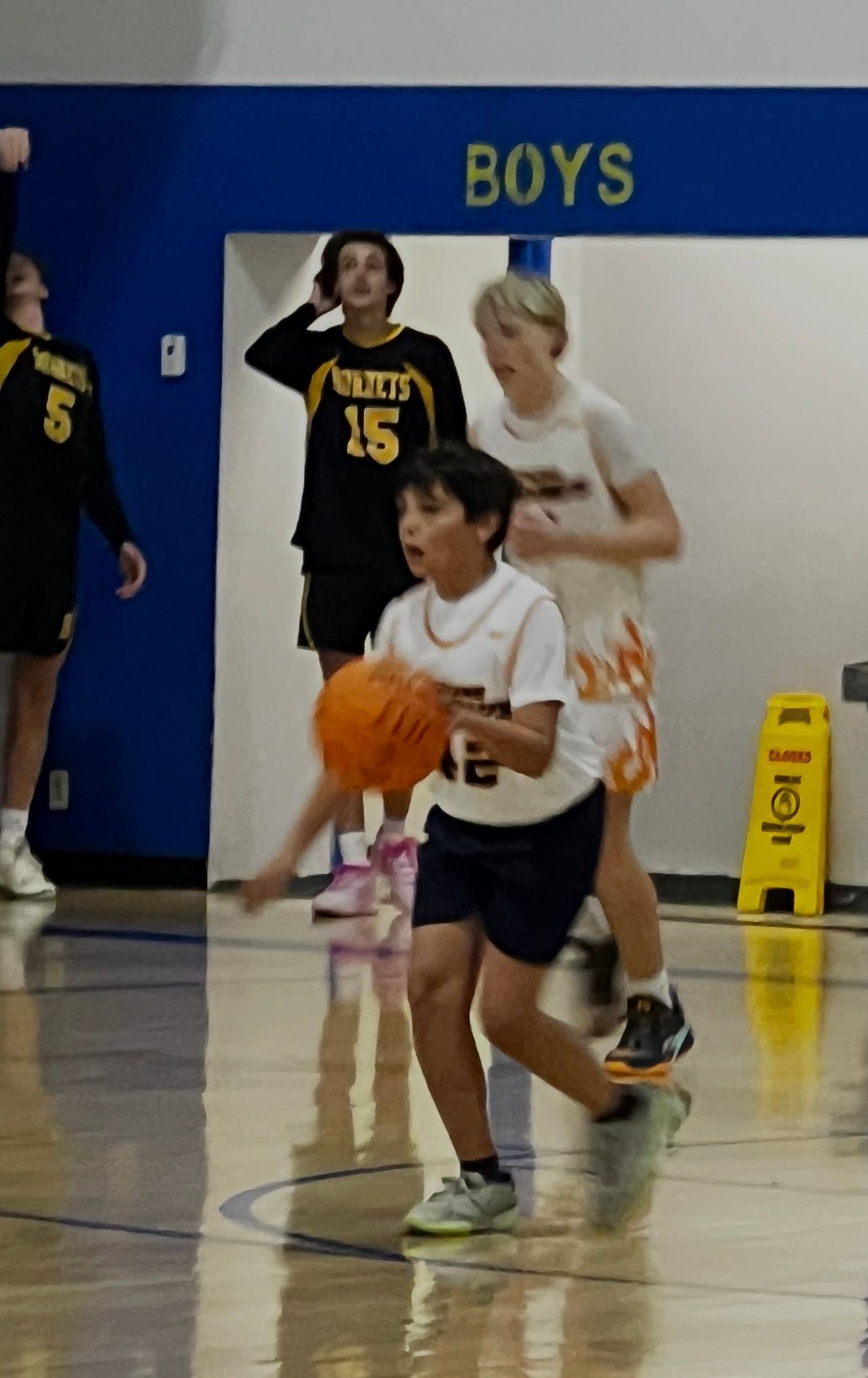 Basketball player dribbling a ball in a gym, two other players nearby, 