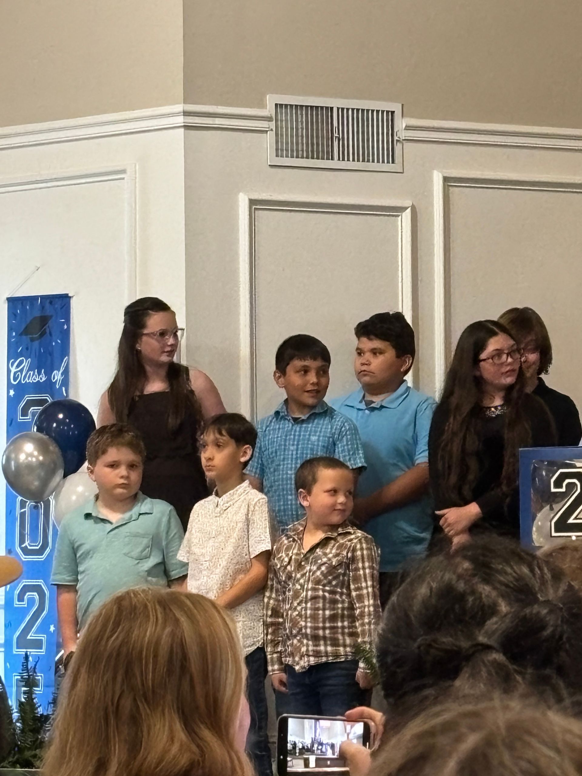 A group of children and adults stand on stage, celebrating a graduation.