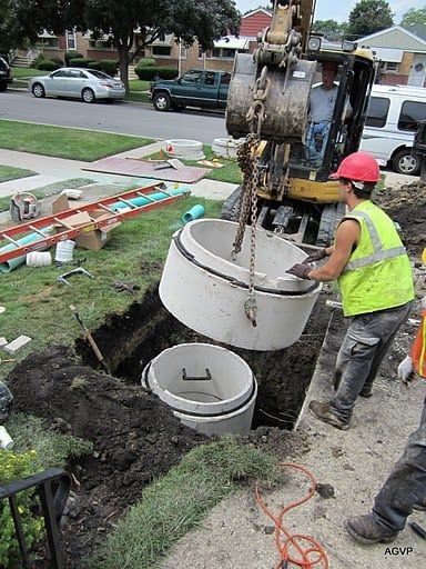 A man is lifting a concrete ring into a hole in the ground.