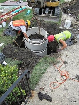 Two construction workers are working on a septic system in the ground.