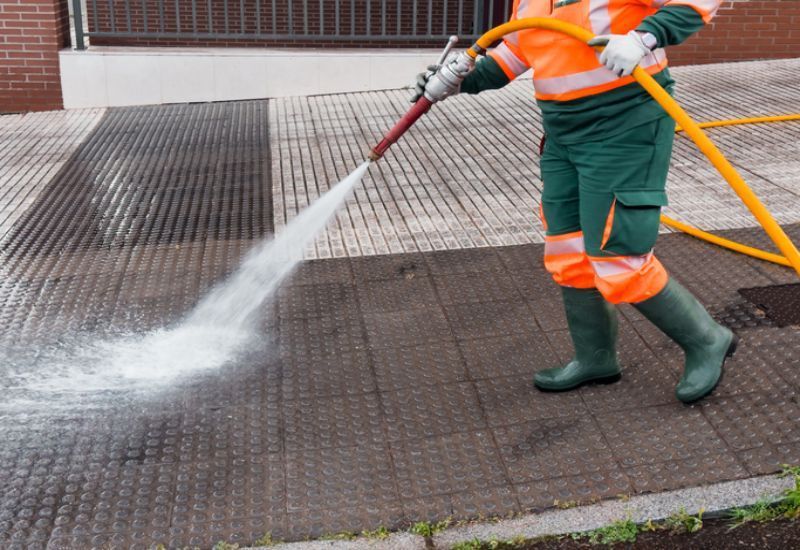 A worker is pressure washing a public sidewalk, showing Hydro Jetting Service in Franklin Park, IL