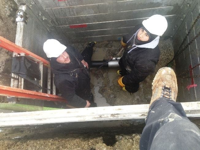 Two men wearing hard hats are working in a hole