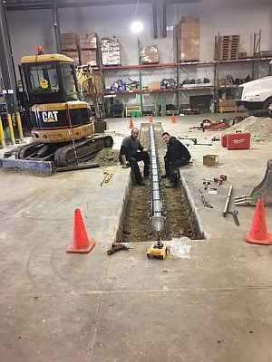 Two men are working on a pipe in a warehouse.