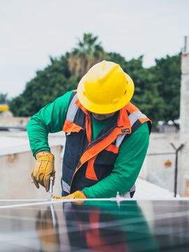 A man wearing a yellow hard hat is working on a solar panel.