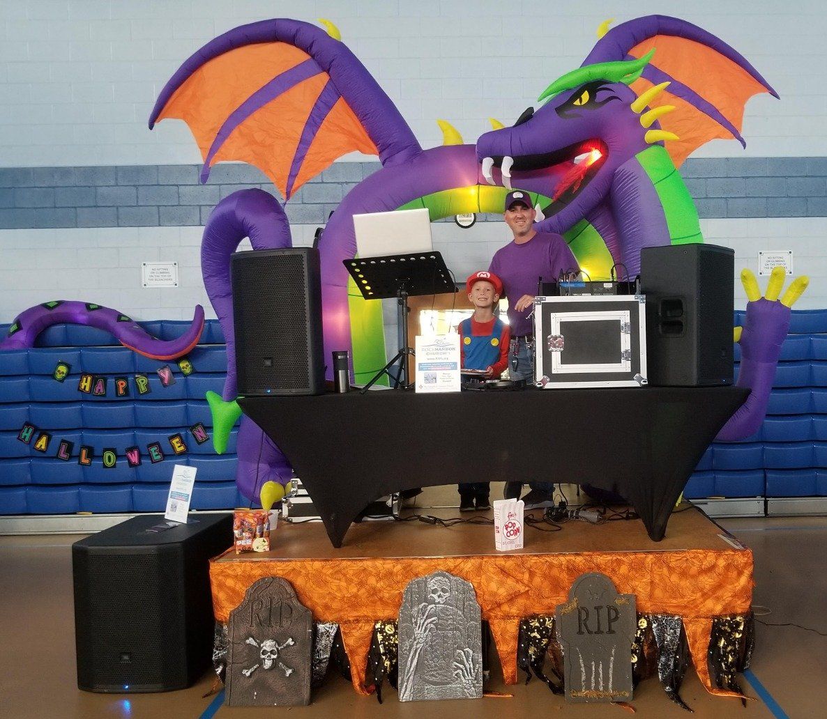 A dj stands behind a table with a large inflatable dragon on it