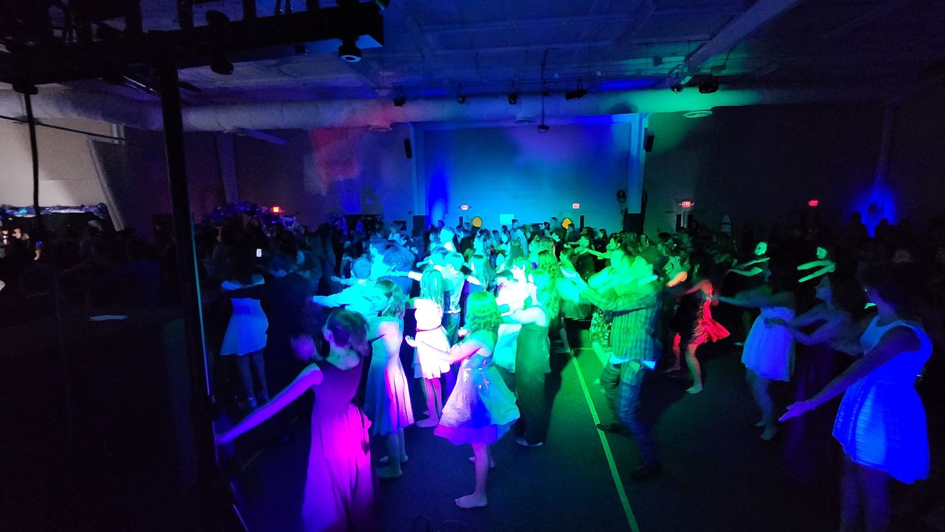 A large group of people are dancing in a dark room with glow in the dark lights.