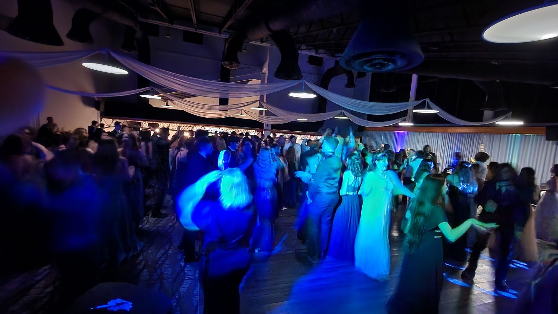 A large group of people are dancing in a dark room with blue lights.
