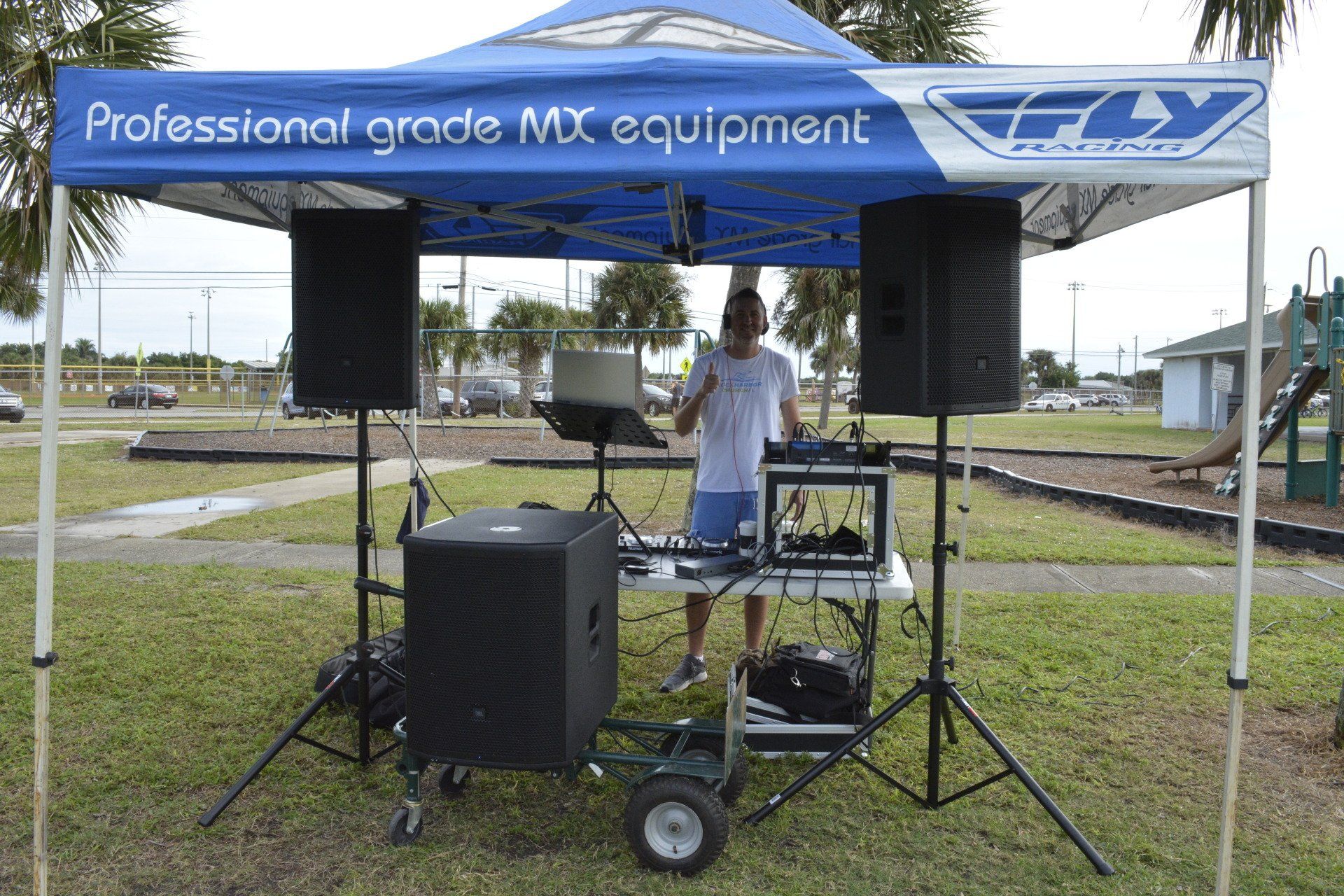 A dj is standing under a blue canopy in a park.